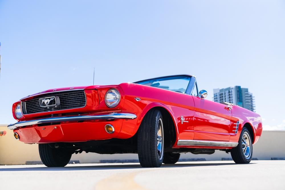 A 1966 Red Mustang. Its parked on the road with a beautiful blue sky and building in the background.